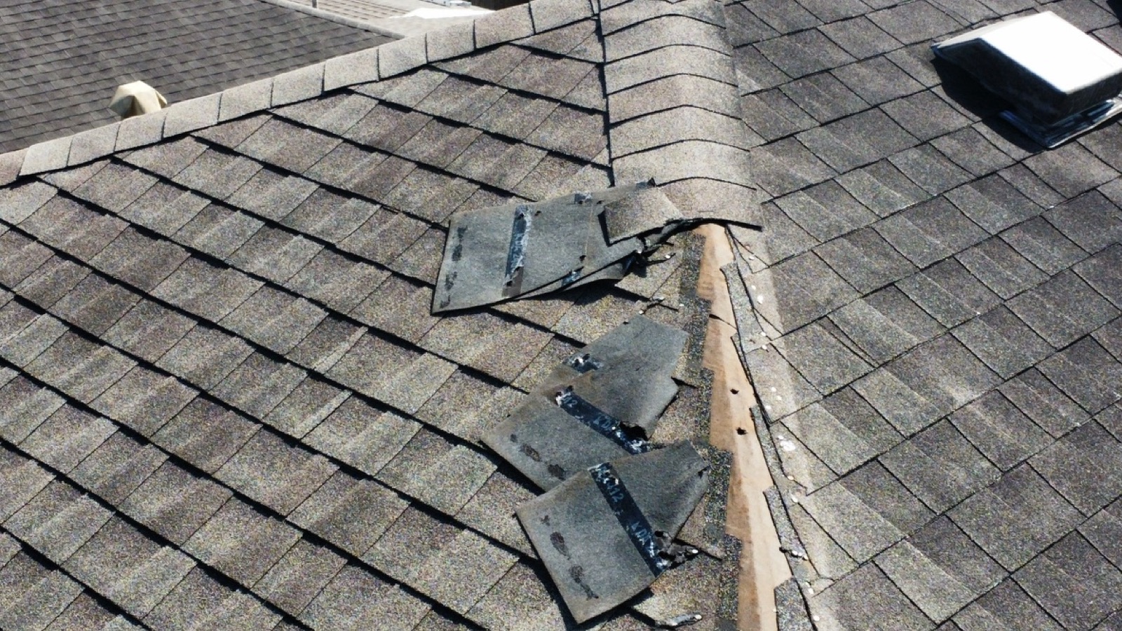 Lifted and torn asphalt shingles near a roof ridge